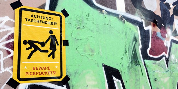 auf einer mit Graffiti besprühten Wand klebt eine Warnung vor Taschendieben