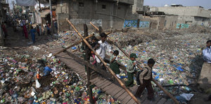 Schulkinder laufen über eine Brücke, die über einen Graben voller Müll führt