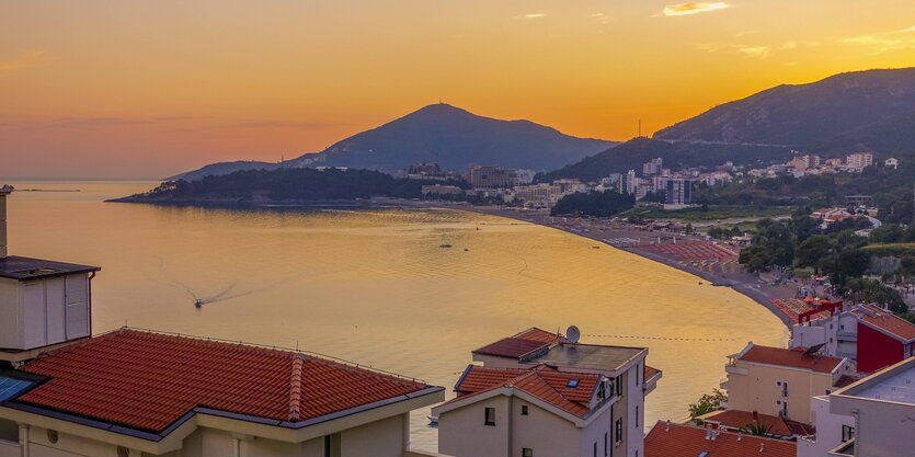 Sonnenuntergang hinter Bergen an der Küste, im Vordergrund klein Häuser