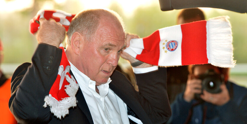 Mann mit fast kahlem Kopf, es ist Uli Hoeneß, wirft sich einen Bayern-Fanschal um