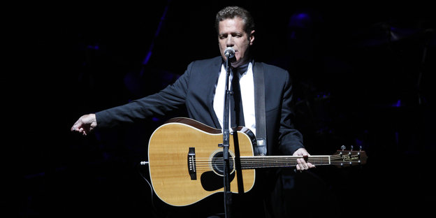 Glenn Frey singt auf der Bühne mit einer Gitarre um die Schulter.