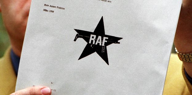 Mensch hält Papier mit RAF-Logo hoch