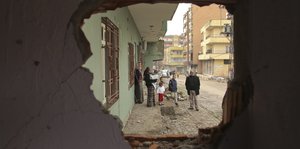 Menschen stehen auf einer staubigen Straße in einer Stadt, Aufnahme durch ein Loch in einer Wand