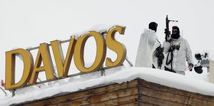 Menschen in weißer Kleidung mit Gewehren in der Hand neben großen Buchstaben "Davos"