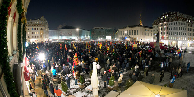 Menschen stehen mit Deutschlandfahnen auf einem Platz in Dresden