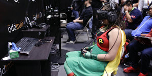 Ein Mädchen im Superheld_innenkostüm von Robin sitzt vor einem Computerspiel