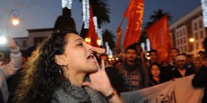 Rufende Demonstrantin vor Fahnenmeer im Nachthimmel von Rabat