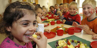 Kinder sitzen am Tisch und essen Obst