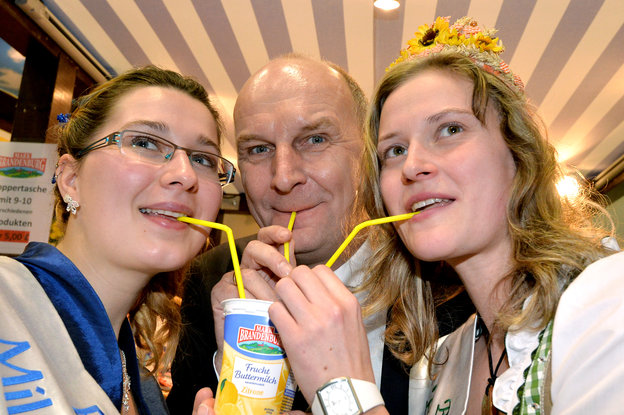 Zwei junge blonde Frauen trinken gemeinsam mit einen Mann eine Buttermilch mit Strohhalmen