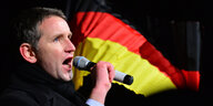 Björn Höcke spricht in ein Mikrofon, im Hintergrund eine Deutschlandfahne.