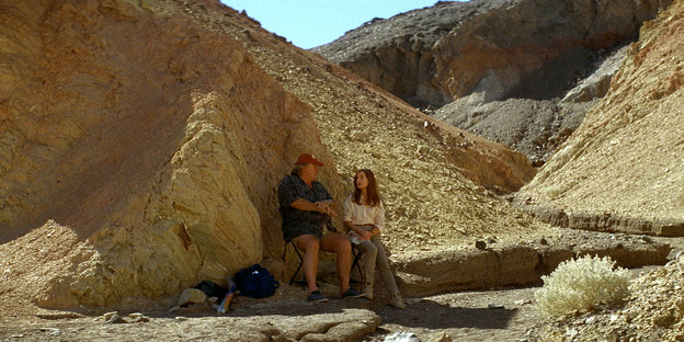 Eine steinige Wüstenlandschaft; klein hocken Isabelle Hupert und Gerard Depardie vor einer Felswand.