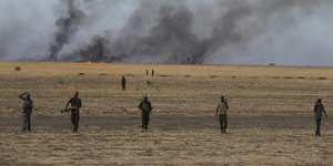 Soldaten laufen über ein Feld, das im Hintergrund brennt