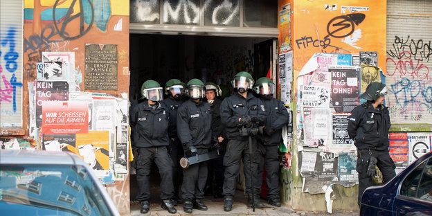 Polizisten stehen dicht gedrängt in der Toreinfahrt eines buntbemalten und mit Plakaten beklebten Hauses