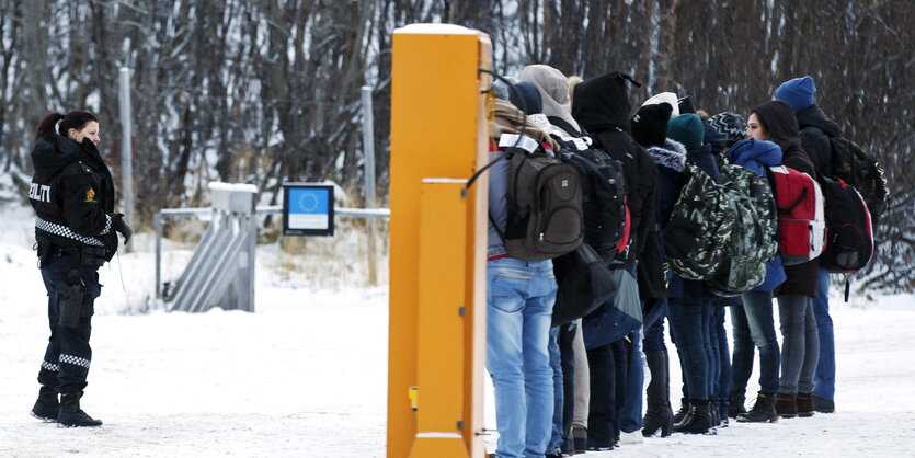 Flüchtlinge stehen im Schnee vor einer Polizistin