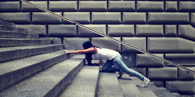 Eine Frau kämpft sich eine Treppe hinauf