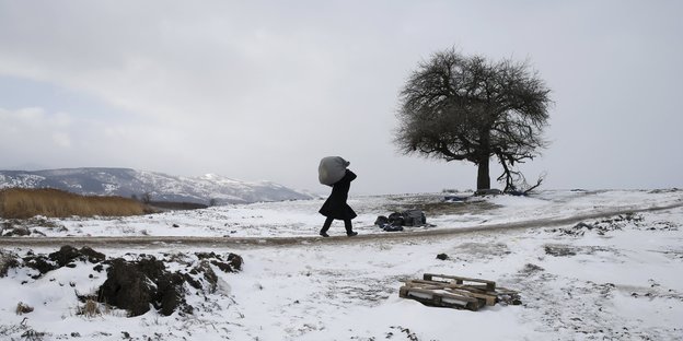 Ein Mann mit einem großen Sack auf den Schultern geht durch eine Winterlandschaft