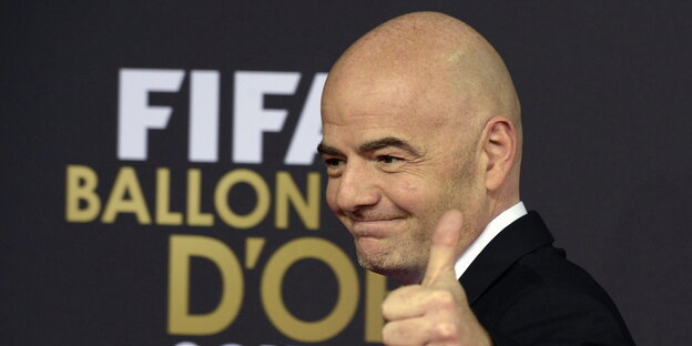 Gianni Infantino grinst und hält den linken Daumen hoch, im Hintergrund das Logo „Fifa Ballon d'Or“
