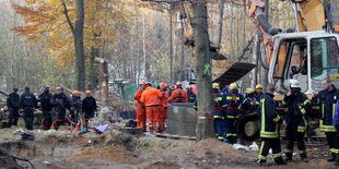 Polizisten und Feuerwehrleute bei einem Bagger im Wald