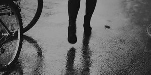 Ausschnitt des Schwarz-weiß-Bildes, der Füße und Waden einer Frau zeigt, die an Fahrradreifen vorbeiläuft
