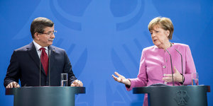 Der türksiche Ministerpräsident Davutoglu und Kanzlerin Merkel sprechen vor blauem Hintergrund.