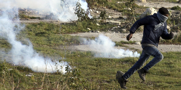 Ein Mann läuft über Rasen durch Tränengasschwaden