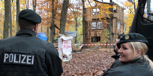 Ein Polizist und eine Polizistin stehen im Hambacher Forst vor einem Holzhäuschen der Besetzer