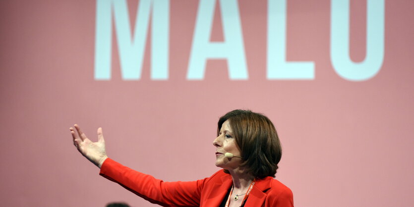 Malu Dreyer mit ausgestrecktem Arm vor einer roten Wand mit dem Schriftzug „Malu“