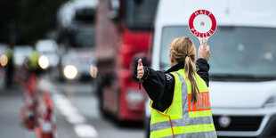 Eine Polizistin in einer gelben Warnweste winkt einen weißen Kleinbus zur Grenkontrollstelle.