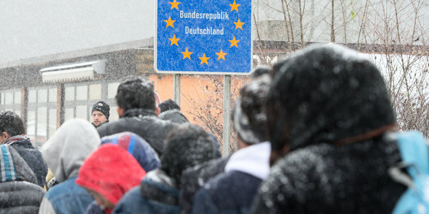 Im Schnee passieren Flüchtlinge mit Kapuzen auf dem Kopf die deutsch-österreichische Grenze