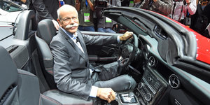 Der Daimler-Chef Dieter Zetsche sitzt am Steuer eines grau-roten Autos und lächelt