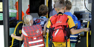 Zwei Schulkinder steigen in einen Bus ein, auf dem Rücken tragen sie Schulranzen
