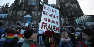 Menschen stehen vor dem Kölner Dom mit einem Schild mit der Aufschrift "Keine Gewalt gegen Frauen"