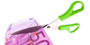 Papierschere mit grünem Griff schneidet 500-Euro-Schein durch.