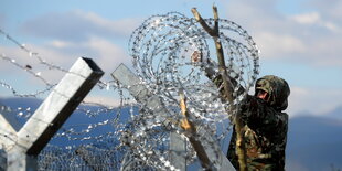 ein Soldat montiert eine Rolle Stacheldraht auf einen Zaun