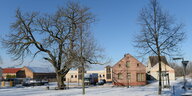 verschneiter Dorfplatz mit Eiche und einige Gebäude
