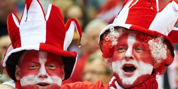 Zwei Männer mit rot-weiß angemalten Gesichtern und rot-weißen Hüten