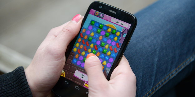 Eine Hand hält ein Smartphone. Auf dem Display ist ein Spiel zu sehen.