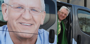 Winfried Kretschmann schaut aus einem Auto, auf das ein Bild von ihm selbst geklebt ist.