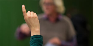 Ein erhobener Zeigefinger, dahinter unscharf ein Lehrer.