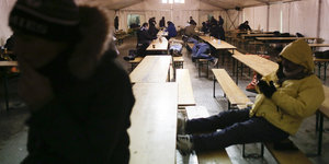 Menschen sitzen in dicken Jacken in einem Zelt