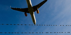 Ein Flugzeug vor blauem Himmel, davor Stacheldraht