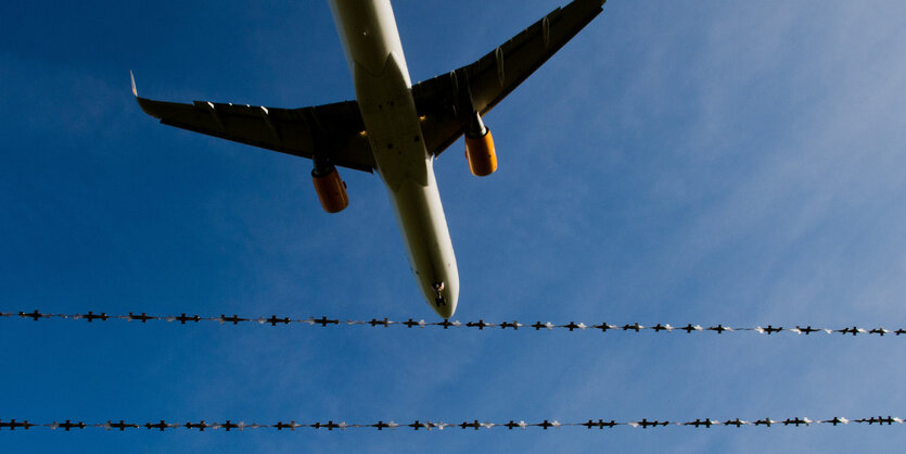 Ein Flugzeug vor blauem Himmel, davor Stacheldraht