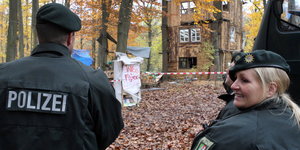 Zwei Polizisten stehen im Wald vor einem Camp von Anti-Braunkohle-Aktivisten.