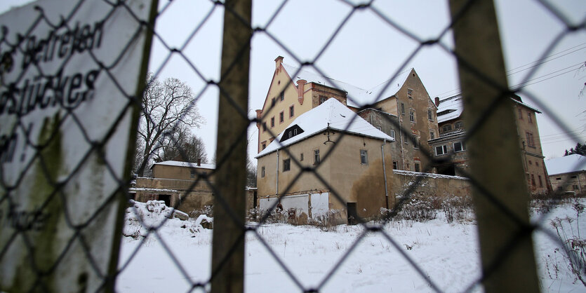 Verschneites Rittergut im Hintergrund. Im Vordergrund ein Zaun.