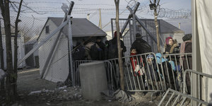 Menschen, darunter Kinder, stehen an einem Grenzübergang mit Stacheldraht und einem kleinen Häuschen