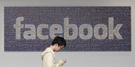 Ein Mann mit Smartphone in der Hand läuft an einem Facebook-Schild vorüber