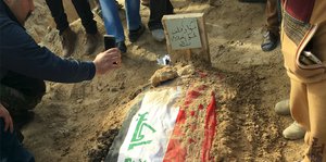 Ein Mann fotografiert ein Grab auf dem eine irakische Flagge niedergelegt ist.