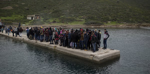 Flüchtlinge stehen auf einem Steg der ins Meer ragt