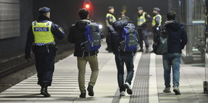 Ein Polizist eskortiert drei Flüchtlinge