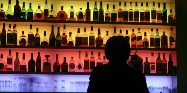 eine Silhoutte an einer Theke, vor buntem Hintergrund Alkohol Flaschen